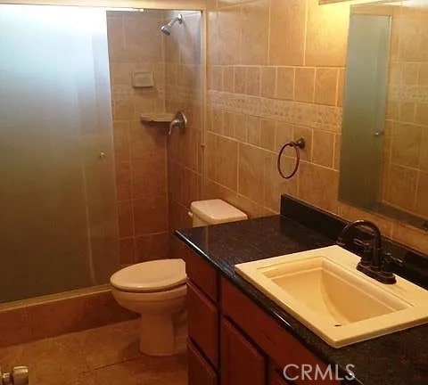 bathroom with tile walls, toilet, a tile shower, tile patterned floors, and vanity