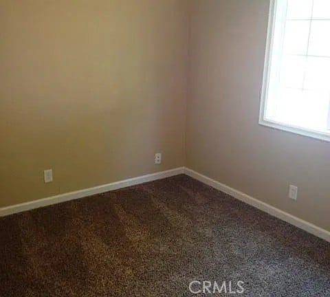 spare room featuring baseboards and dark colored carpet