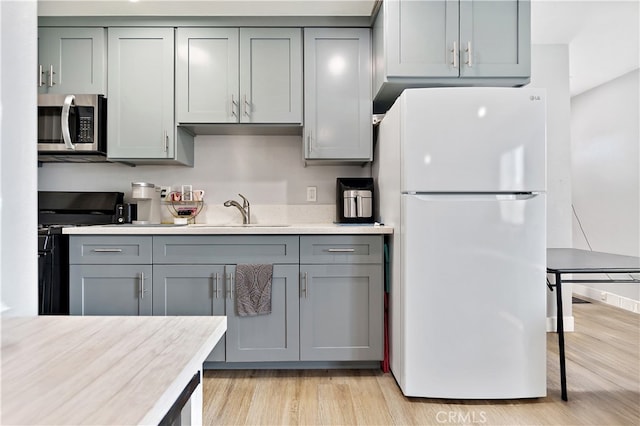 1301 E Pacific Coast, Wilmington, CA 90744 - kitchen with freestanding refrigerator, stainless steel microwave, black gas range oven, gray cabinetry, and a sink