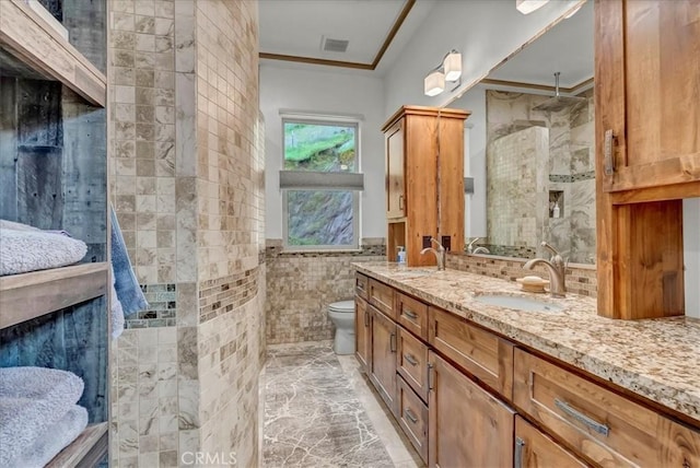 full bathroom featuring a tile shower, a sink, tile walls, crown molding, and visible vents