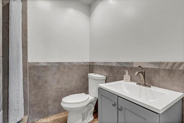 bathroom featuring tile walls, toilet, vanity, a wainscoted wall, and wood finished floors