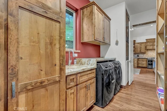 washroom with washing machine and clothes dryer, cabinet space, a sink, and light wood-type flooring