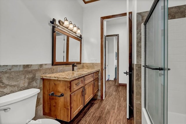 full bath featuring toilet, wood finished floors, a tile shower, tile walls, and vanity