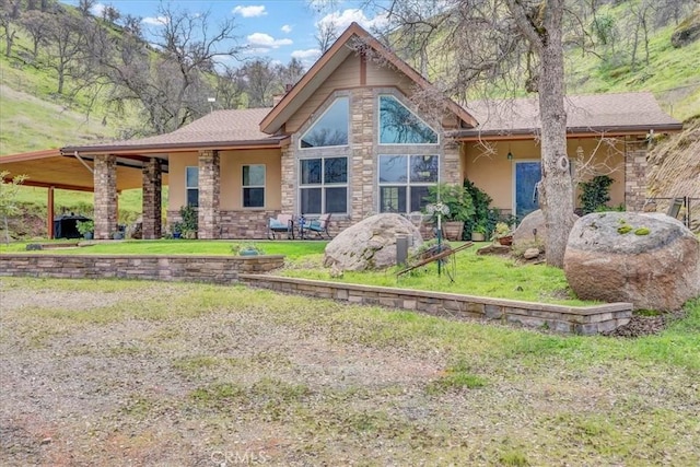 back of property with a lawn, stone siding, and stucco siding