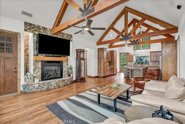 living area featuring beam ceiling, visible vents, wood finished floors, and a stone fireplace