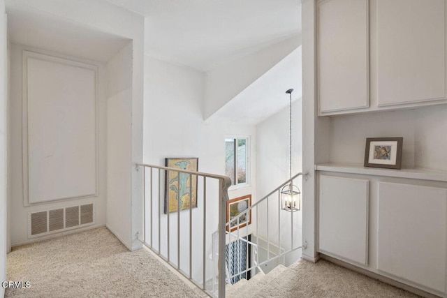 hallway featuring carpet, visible vents, an upstairs landing, and a notable chandelier