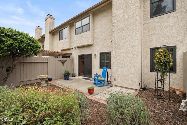 rear view of house with a patio area, stucco siding, and fence