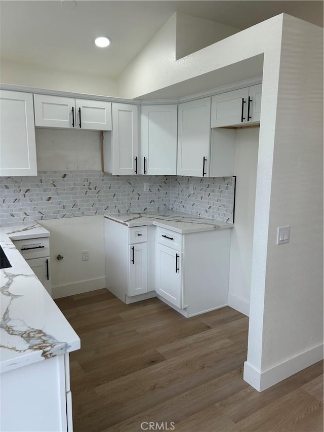 kitchen featuring light stone counters, wood finished floors, baseboards, and backsplash