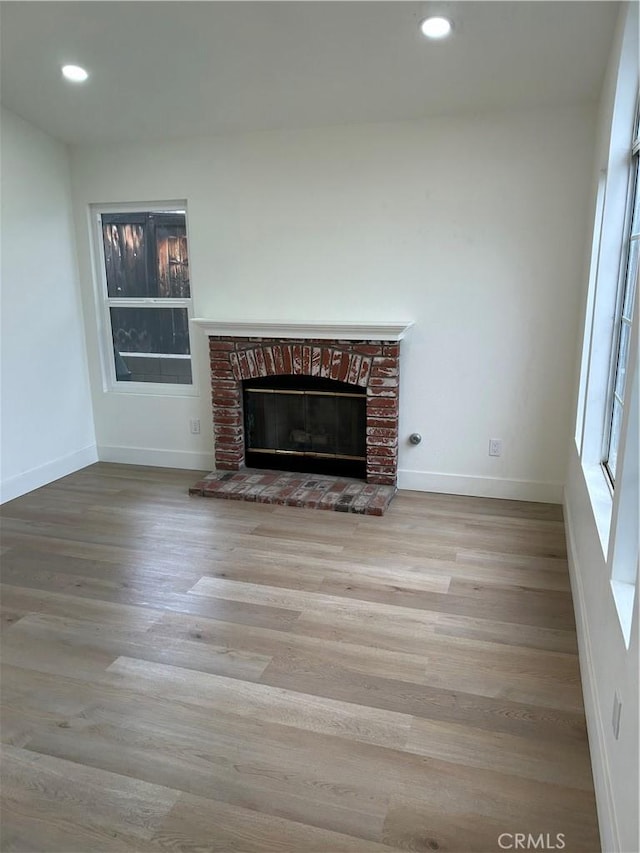unfurnished living room with wood finished floors, baseboards, a brick fireplace, and recessed lighting
