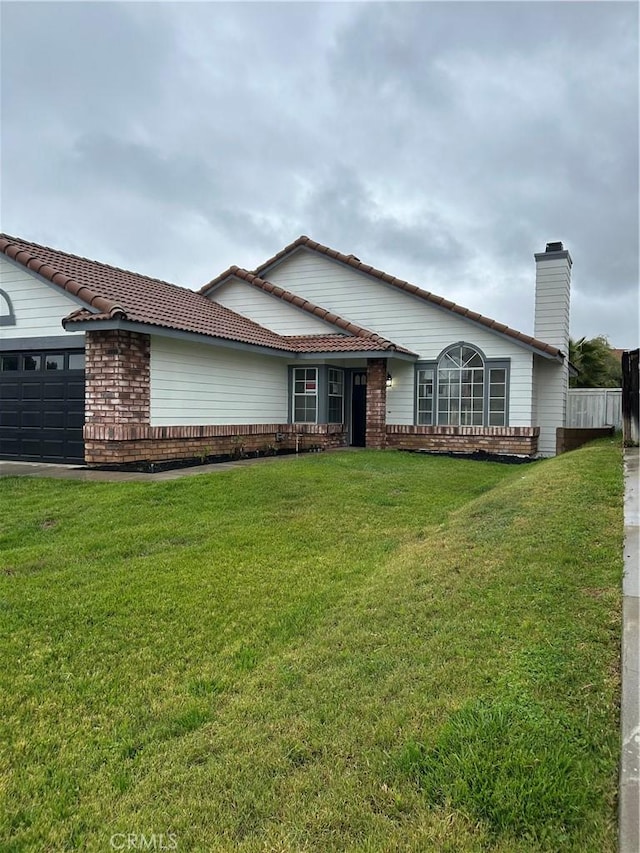 ranch-style home featuring an attached garage, brick siding, a chimney, and a front yard