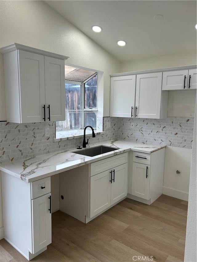 kitchen with a sink, light stone counters, decorative backsplash, and light wood-type flooring