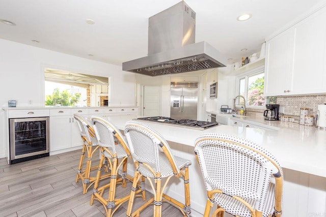 kitchen featuring built in appliances, light countertops, range hood, and beverage cooler