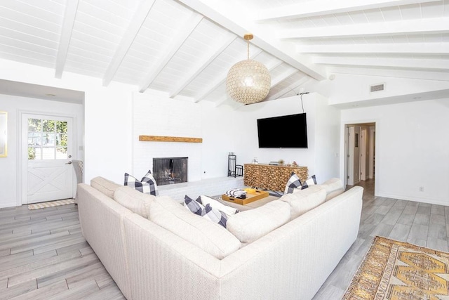 living area with light wood-style floors, visible vents, a fireplace, and vaulted ceiling with beams