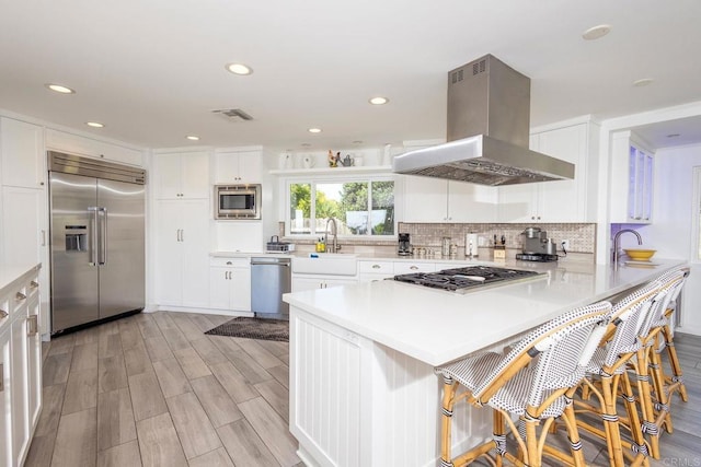 kitchen with a peninsula, island range hood, white cabinets, visible vents, and built in appliances
