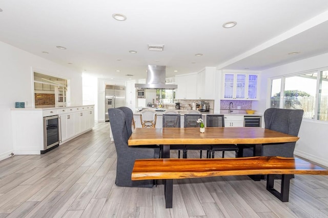 dining room with light wood-style floors, a wealth of natural light, and beverage cooler