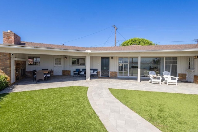 back of property featuring a lawn, a patio area, a chimney, and board and batten siding