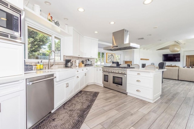 kitchen with a sink, a peninsula, open floor plan, range hood, and appliances with stainless steel finishes