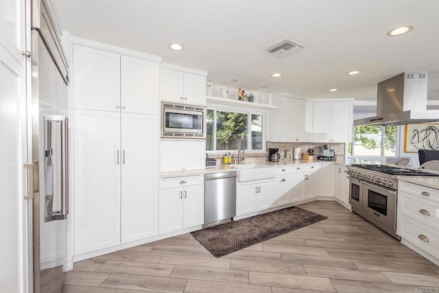 kitchen with a sink, wall chimney exhaust hood, white cabinets, visible vents, and built in appliances