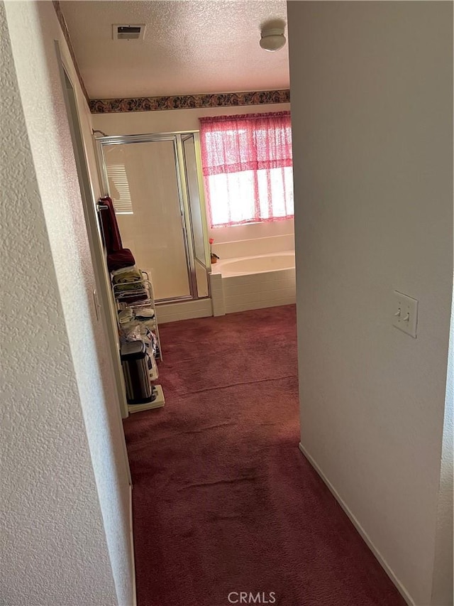 corridor with a textured ceiling, a textured wall, carpet floors, and visible vents