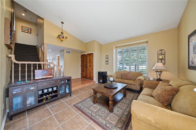 living area with tile patterned floors, vaulted ceiling, visible vents, and stairs