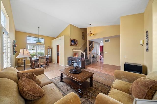tiled living room featuring a chandelier, high vaulted ceiling, visible vents, and stairs
