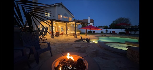 pool at twilight featuring an outdoor living space with a fire pit, a patio, a pool with connected hot tub, and a fenced backyard