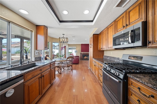 kitchen featuring light wood-style flooring, a sink, brown cabinetry, a glass covered fireplace, and appliances with stainless steel finishes