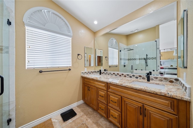 full bath featuring a stall shower, baseboards, double vanity, and a sink