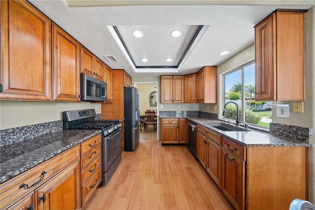 kitchen with appliances with stainless steel finishes, brown cabinetry, visible vents, a sink, and light wood-type flooring