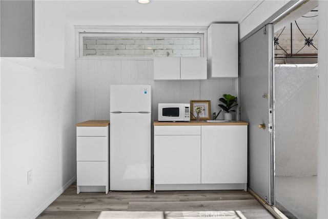 kitchen featuring white cabinetry, light wood finished floors, white appliances, and a sink