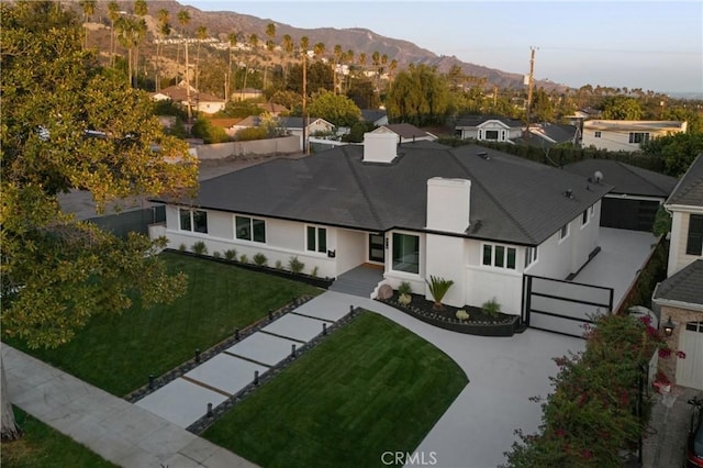 exterior space featuring a chimney, a mountain view, stucco siding, a shingled roof, and a front yard