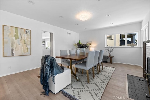 dining area with a fireplace, baseboards, visible vents, and light wood-style floors