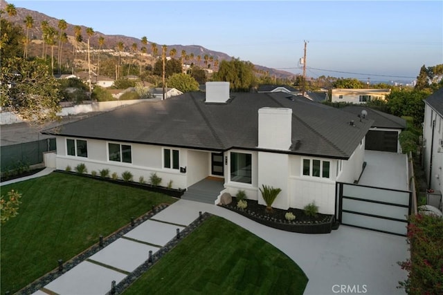 ranch-style home with a front lawn, a shingled roof, fence, and a mountain view