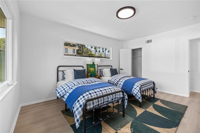 bedroom with multiple windows, visible vents, wood finished floors, and baseboards