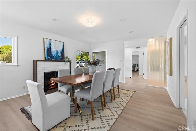 dining room with light wood-style floors, a brick fireplace, baseboards, and a healthy amount of sunlight