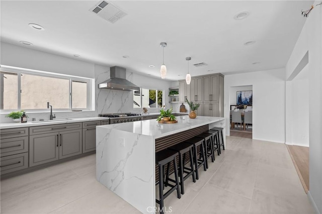kitchen with wall chimney exhaust hood, gray cabinets, visible vents, and a sink
