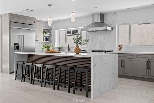 kitchen featuring stainless steel built in fridge, open shelves, decorative backsplash, wall chimney range hood, and gray cabinets