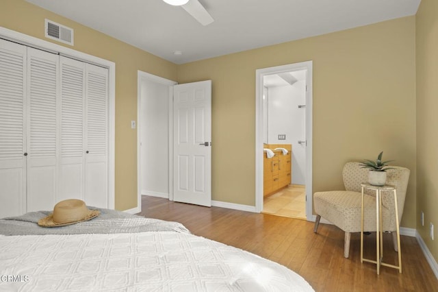 bedroom with a closet, wood finished floors, ensuite bath, visible vents, and baseboards