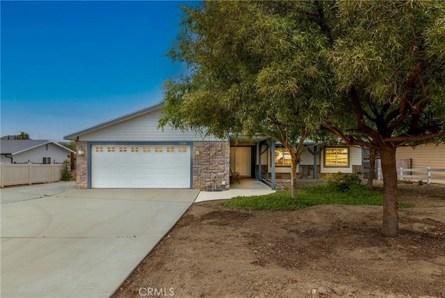 view of front of home featuring stone siding, concrete driveway, fence, and a garage