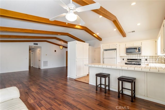 kitchen featuring a peninsula, freestanding refrigerator, vaulted ceiling with beams, stove, and stainless steel microwave