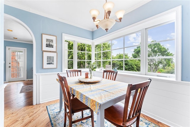 dining space featuring a wainscoted wall, ornamental molding, light wood-type flooring, a chandelier, and arched walkways