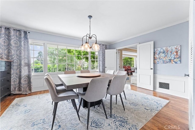 dining space featuring wainscoting, crown molding, visible vents, and wood finished floors