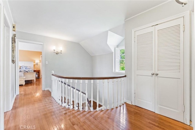 corridor featuring baseboards, hardwood / wood-style floors, an upstairs landing, and lofted ceiling