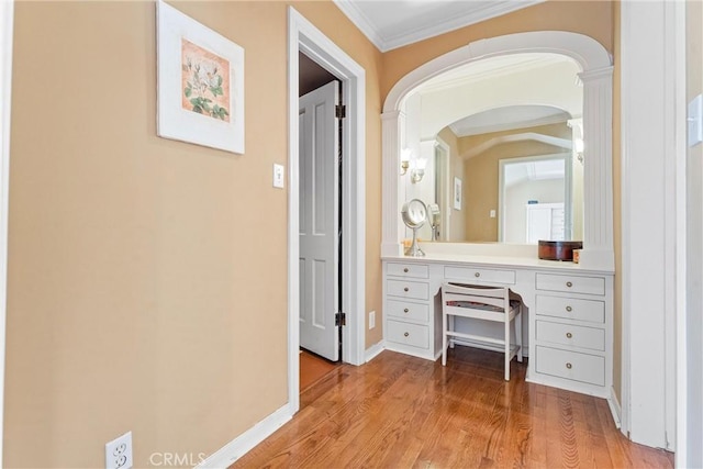 corridor with light wood finished floors, decorative columns, crown molding, baseboards, and arched walkways