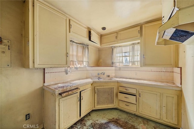 kitchen with a sink, tile counters, cream cabinetry, under cabinet range hood, and tasteful backsplash