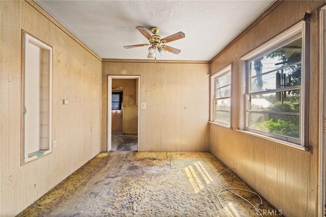 empty room featuring ceiling fan, wooden walls, and crown molding