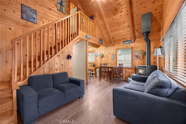 living room featuring stairs, lofted ceiling with beams, wood finished floors, a wood stove, and wooden walls