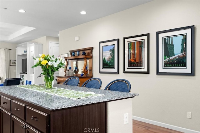 kitchen with a center island, dark brown cabinetry, baseboards, light wood-style floors, and light stone counters