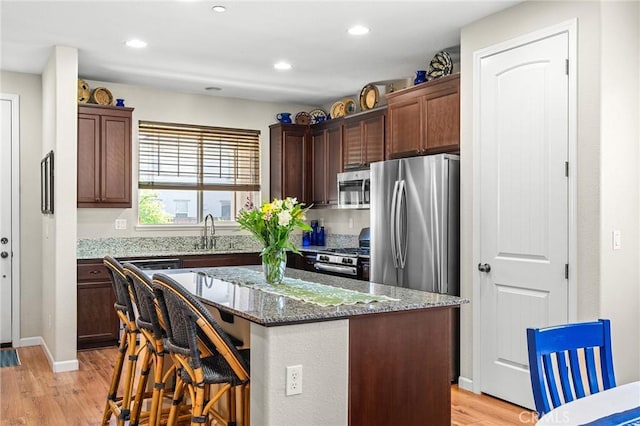 kitchen featuring a sink, stainless steel appliances, dark stone counters, a kitchen breakfast bar, and light wood-type flooring