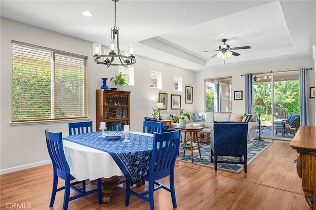 dining space featuring ceiling fan with notable chandelier, light wood-type flooring, baseboards, a raised ceiling, and recessed lighting